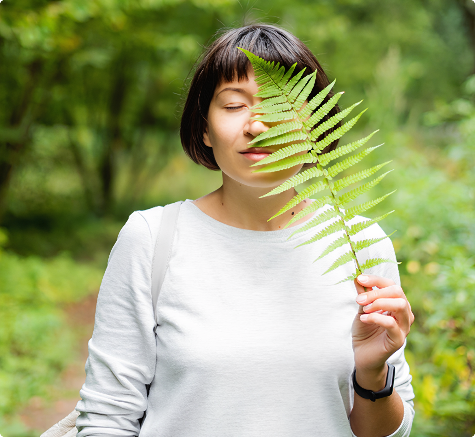 Woman holding fern leaf in forest.