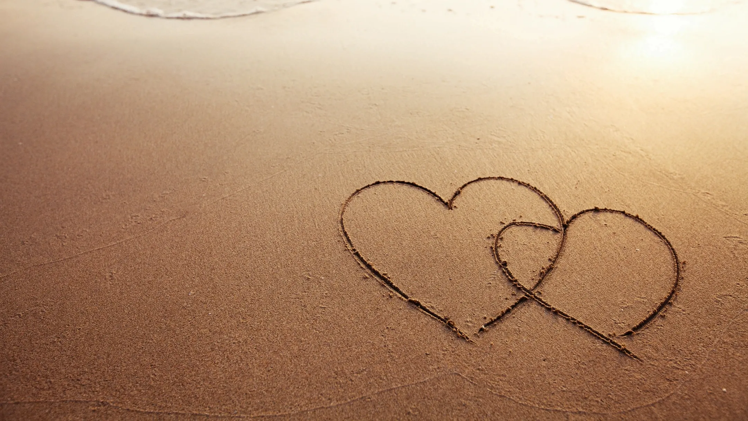 Interlocking hearts drawn on sandy beach.