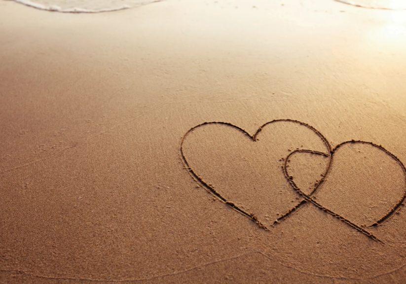 Interlocking hearts drawn on sandy beach.