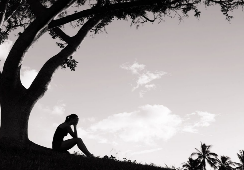 Silhouette of person sitting under a tree.